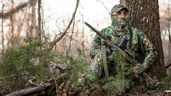 Man in camouflage leaned against a tree hunting turkeys