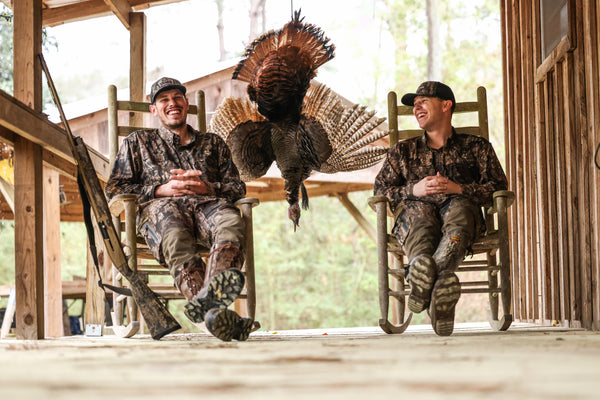 Two hunters sitting on a porch in front of a turkey