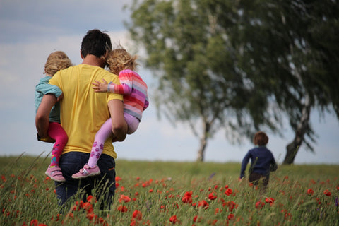 man carrying two toddlers through a poppy field