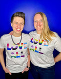 LP with their wife standing in front of a blue background - both are wearing white Dash of Pride LOVE ALL tees