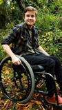 Logan in his wheelchair outside at the park with leaves on the ground.