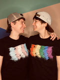 The Ariels - two white woman with short hair with hats backwards wearing Dash of Pride Tees (transgender and rainbow scribble)