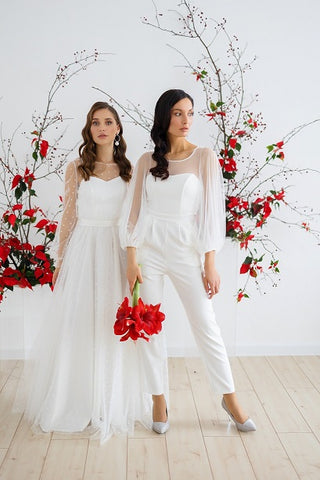 Two brides on their wedding day; one bride wearing a wedding dress; one bride wearing a wedding jumpsuit