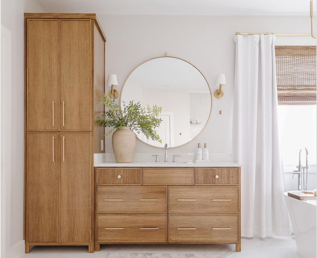 Baño decorado al estilo escandinavo con muebles minimalistas y funcionales, un espejo circular al centro y lámparas minimalistas de siluetas suaves de la marca Visual Comfort & Co.