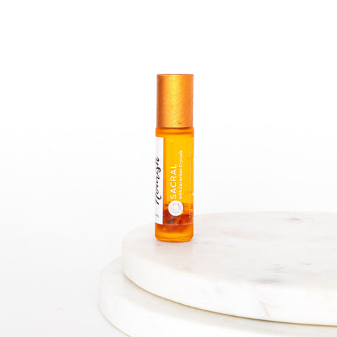 Sacral Roller Blend in an orange bottle with a gold cap on a white circular marble platform