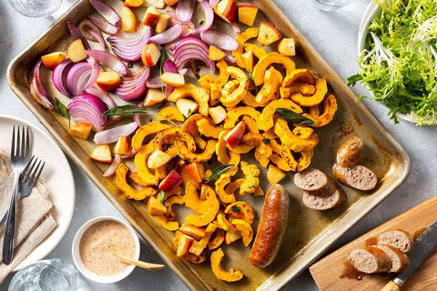A large sheet pan with sliced apples, squash and sausages ready for roasting