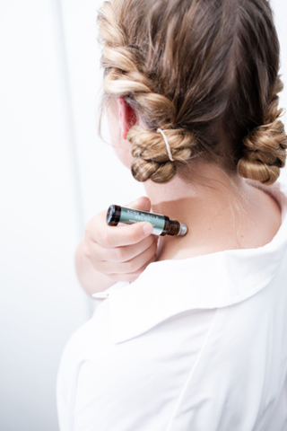 a woman rubbing sore muscle roller blend on her left shoulder back area