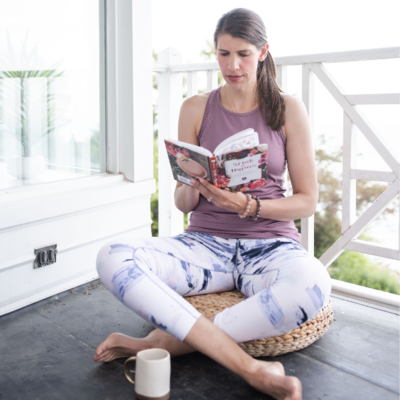 Jamie reading sitting cross legged on a deck  with a coffee mug