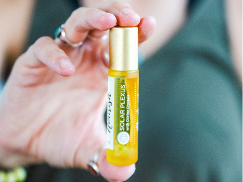 the solar plexus roller blend held in a hand in front of a woman wearing a green tank top