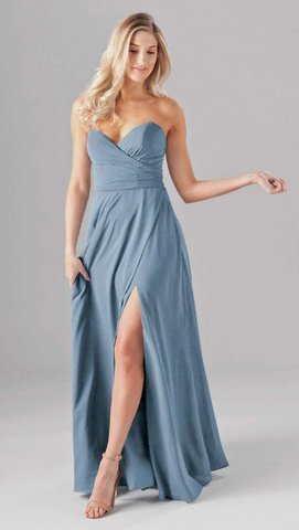 Kennedy Blue model wearing a romantic gown with a sweetheart neckline and ruched bodice, and a flowy skirt with a side slit.