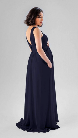 Kennedy Blue model wearing a flowy maternity dress with a v-neckline and pleated bodice.