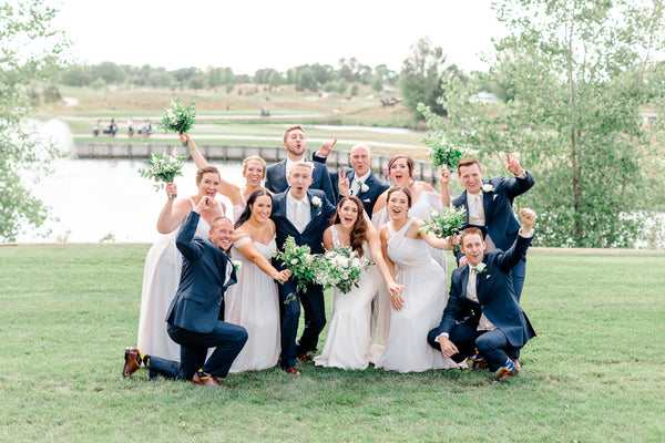 Bridal party gathered on a golf course cheering and throwing their hands in the air.