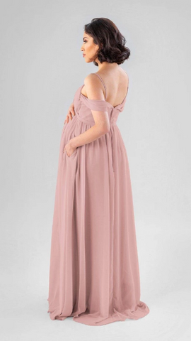 Kennedy Blue model wearing a maternity dress with a romantic neckline and long flowy skirt. 