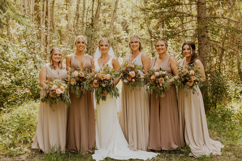 Bride and Bridesmaids posing in front of a wooded greenery background.