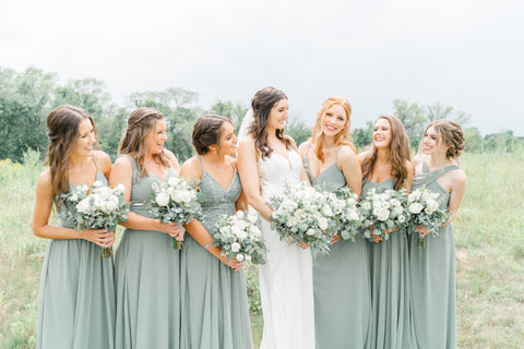 Bride and Bridesmaids looking at each other and smiling. They are standing in a beautiful green field. 