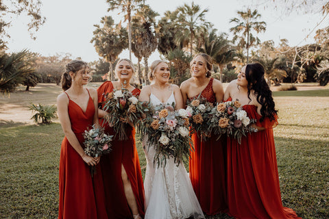 Bride and Bridesmaids laughing as they look around at each other. The background is a beautiful area with palm trees. 