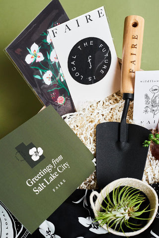 Close up of a custom corporate gift box featuring Faire branded patch, etched garden trowel, greeting card reading "Greetings from Salt Lake City" and live air plant