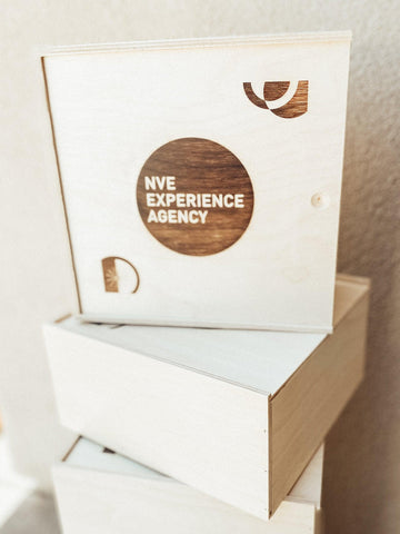 Custom branded wooden slide top boxes lay stacked, featuring NVE Experience agency logo and geometric shapes