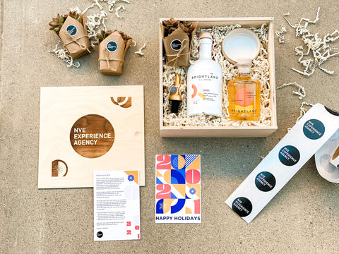 A custom gift box contains lays spread out on the concrete - a wooden gift box, custom black and white shipping tape, a holiday card, olive oil and other homegoods