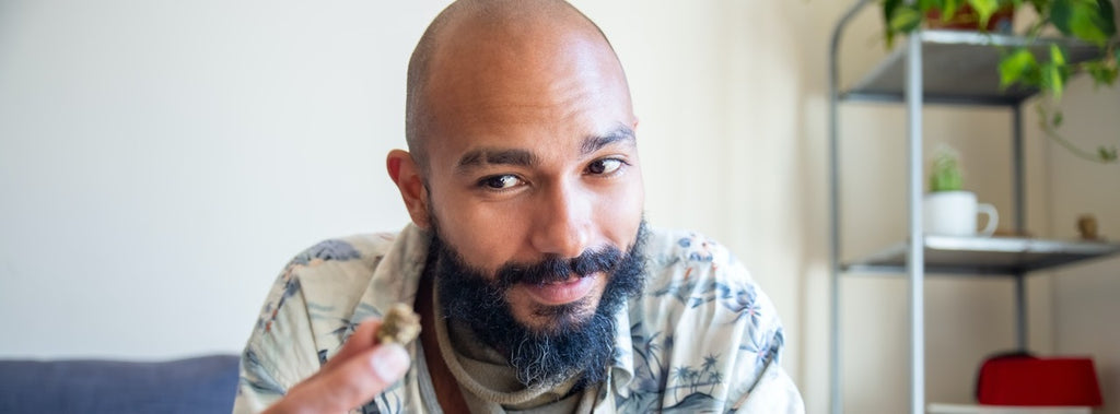 Person smiling and holding a bud of dry herb