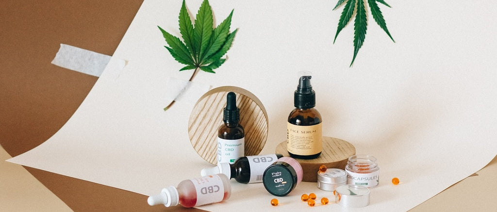 An array of cannabis concentrates: CBD oil, capsules, and topicals, with marijuana leaves in the backround.