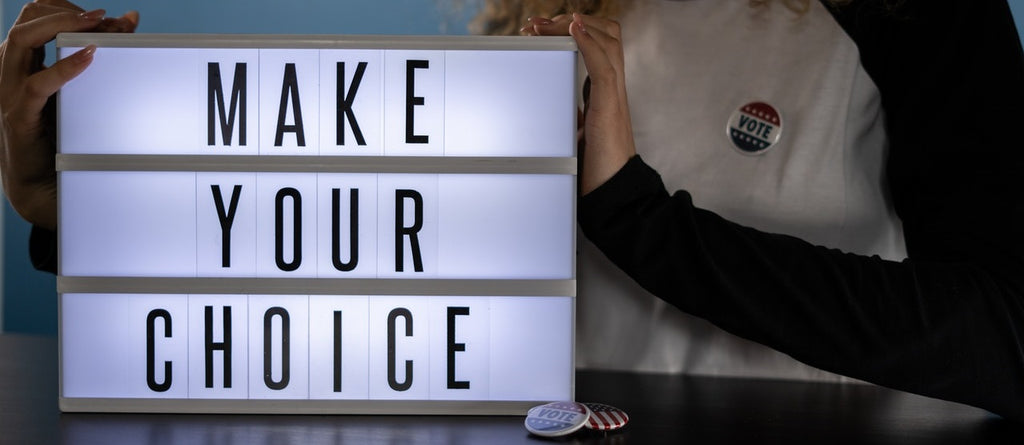 An illuminated sign saying "MAKE YOUR CHOICE" beside a person with a button that says "VOTE".