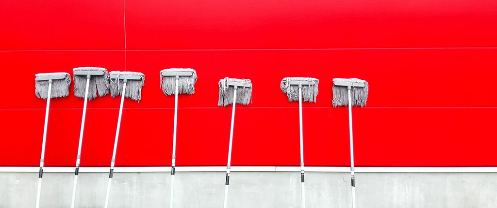 A row of mops or cleaning brushes against a wall.