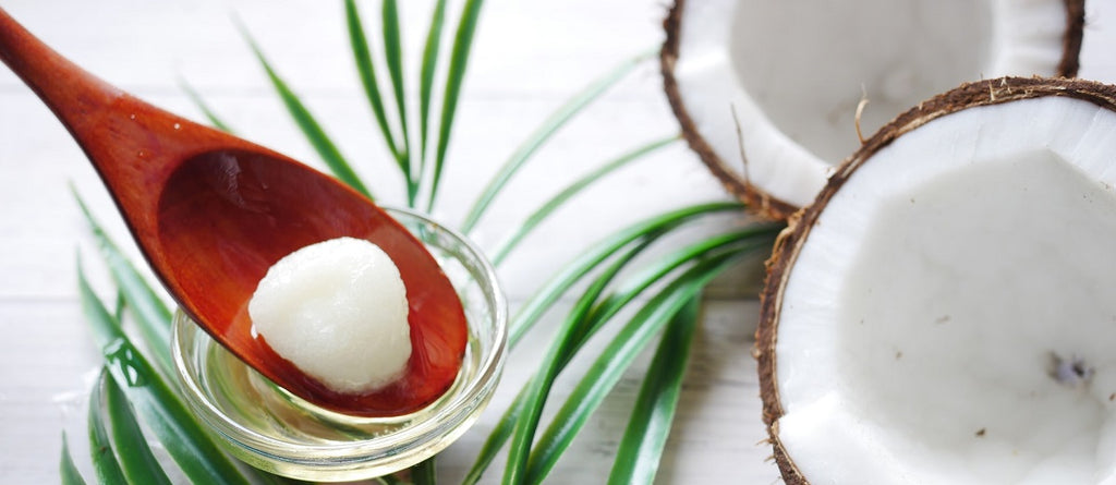 A spoon with a piece of coconut in a dish of coconut oil, beside a coconut sliced in half.