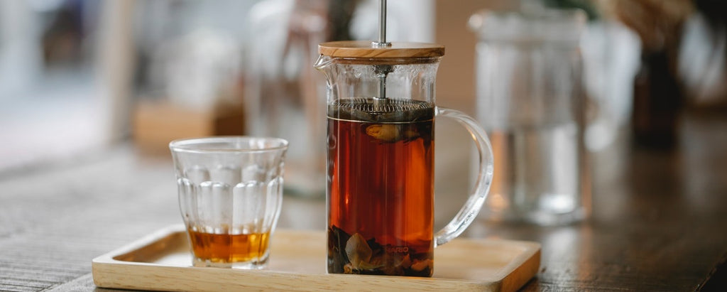 A french press filled with tea and herbs steeping.