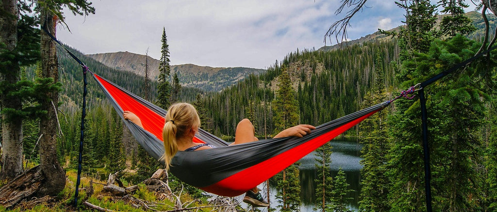 A personal relaxing in a hammock outside by a lake.