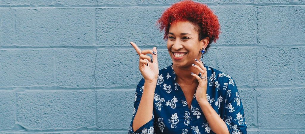 Happy person smiling against a wall, pointing their finger.