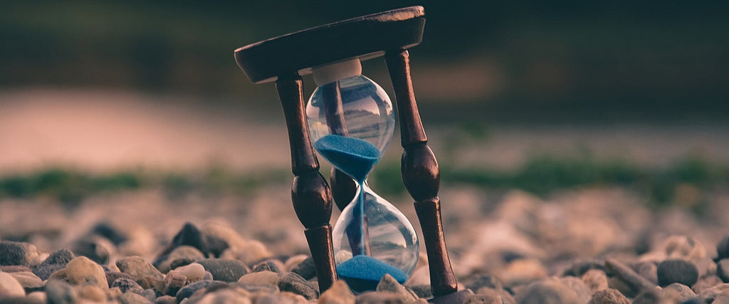 An hourglass measuring time with blue sand on a rocky beach.