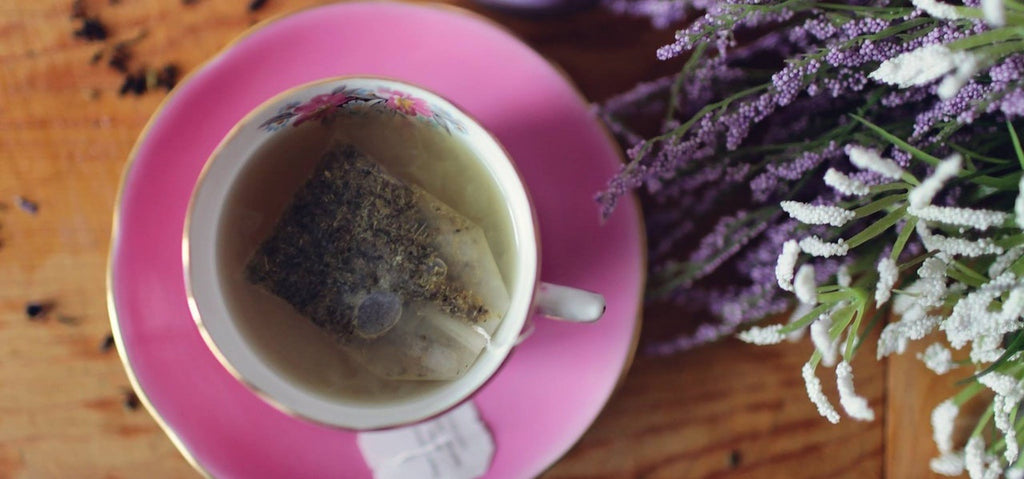A cup of green tea beside some dried lavender herbs. 