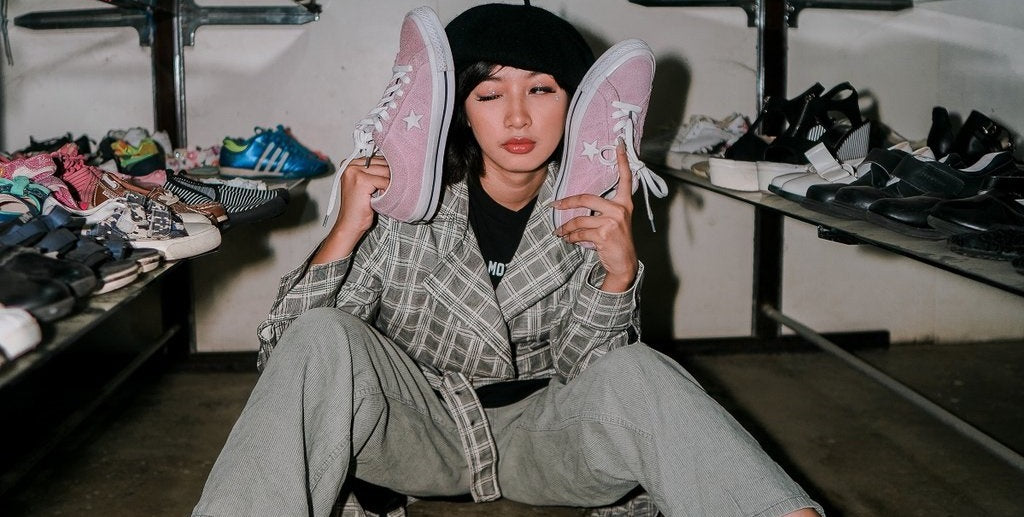 Person sitting in closet near shoes, choosing a pair of shoes and holding a pair against their face.