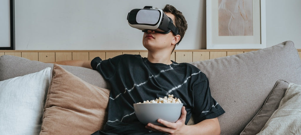 Person wearing VR goggles sitting on a couch with a bowl of popcorn.