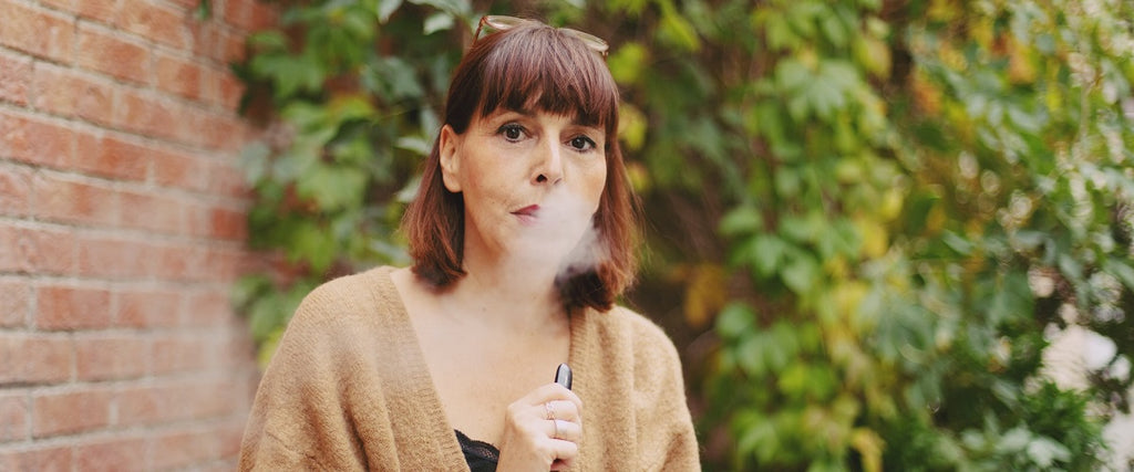 Person using a vape outside, exhaling vapor