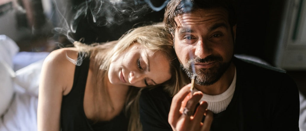 Two stoned people smoking a joint on a bed.