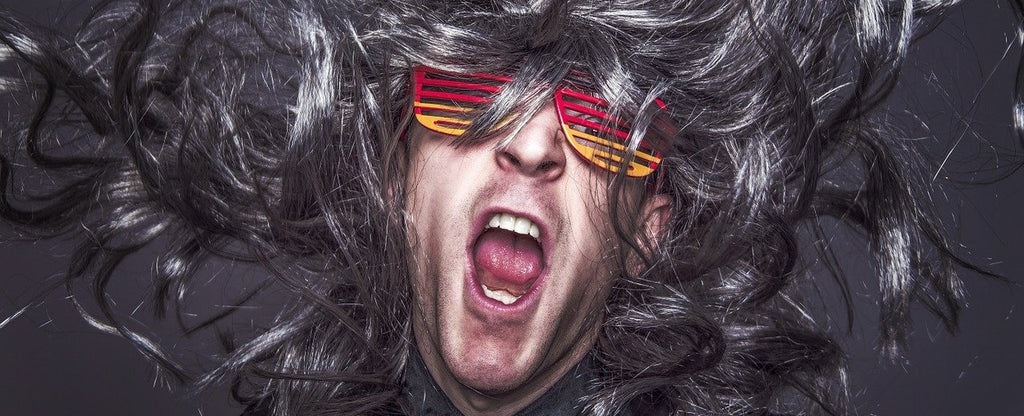 A person wearing multicolored glasses, with wild hair, mouth open as if yelling.