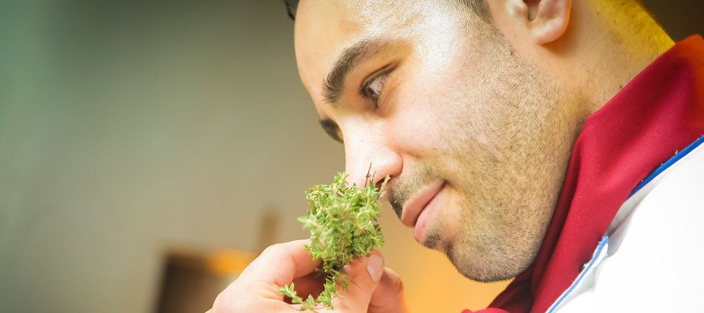 A chef smelling a green herb.