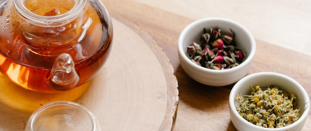 A transparent pot of black tea on a table with bowls of tea ingredients to add.