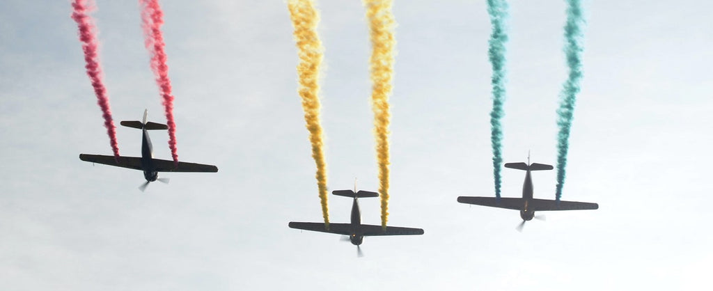 Three airplanes flying across the sky, with colored vapor trails.