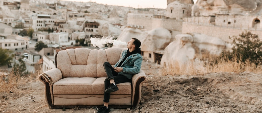 Person vaping on a sofa outside.