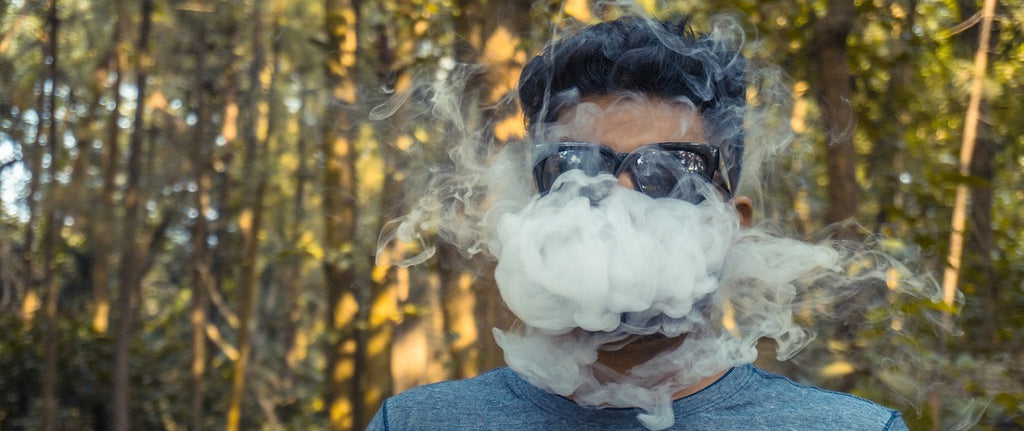 A person vaping dry herb in a forest.