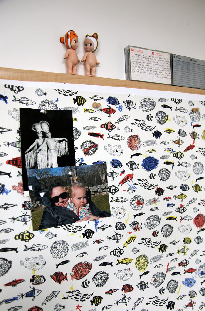 Fish patterned wallpaper surrounded by photographs, kewpie dolls, and cassette tapes