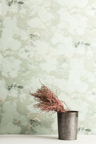 Flat Vernacular's wallpaper Perennial in the color way Lichen, a sage green floral pattern. Placed in front of the wallpaper is a red bouquet in a metal pot.