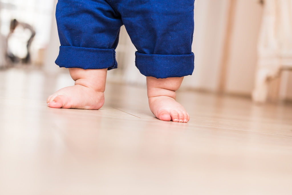 Foto de pies de bebé caminando descalzo con pantalón azul navy
