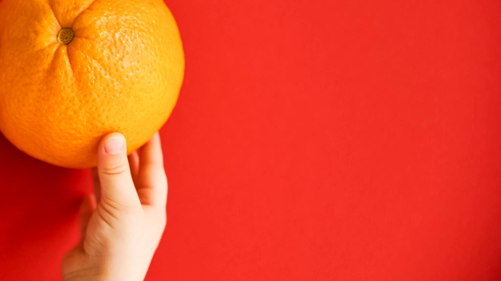 Foto de manos de bebé tomando una naranja sobre mesa roja