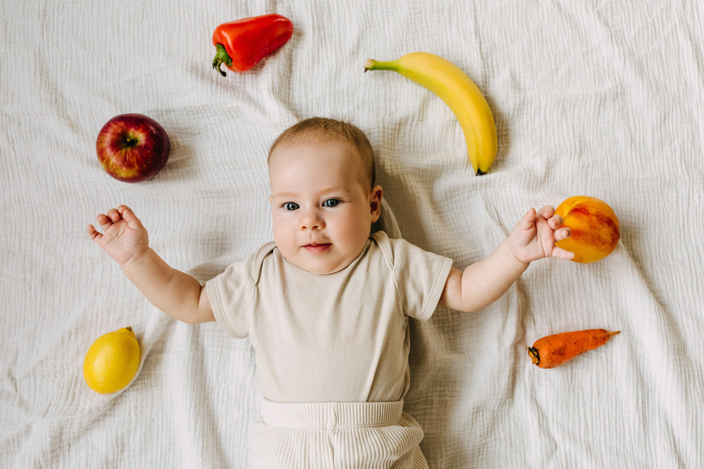 Foto de bebé acostado y rodeado de frutas sobre cama