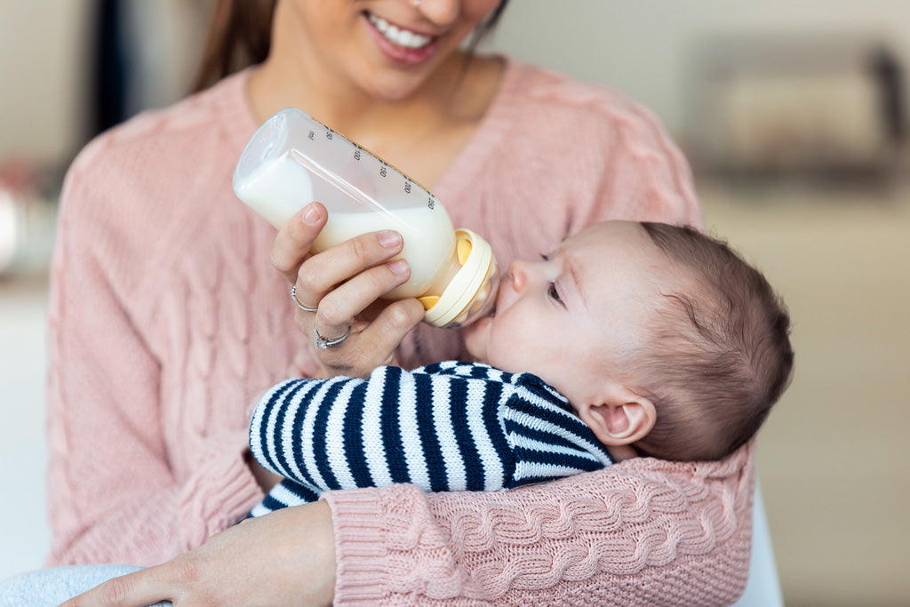 Foto de mamá con bebé en sus brazos alimentando dando leche en biberón