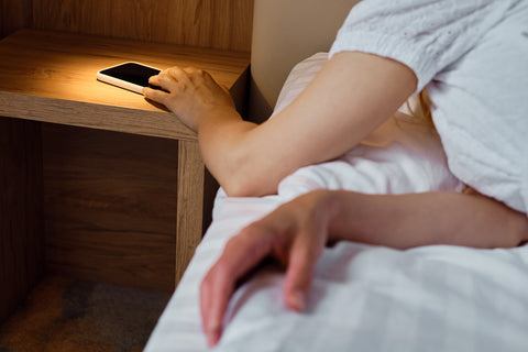 hand reaching for cell phone on nightstand